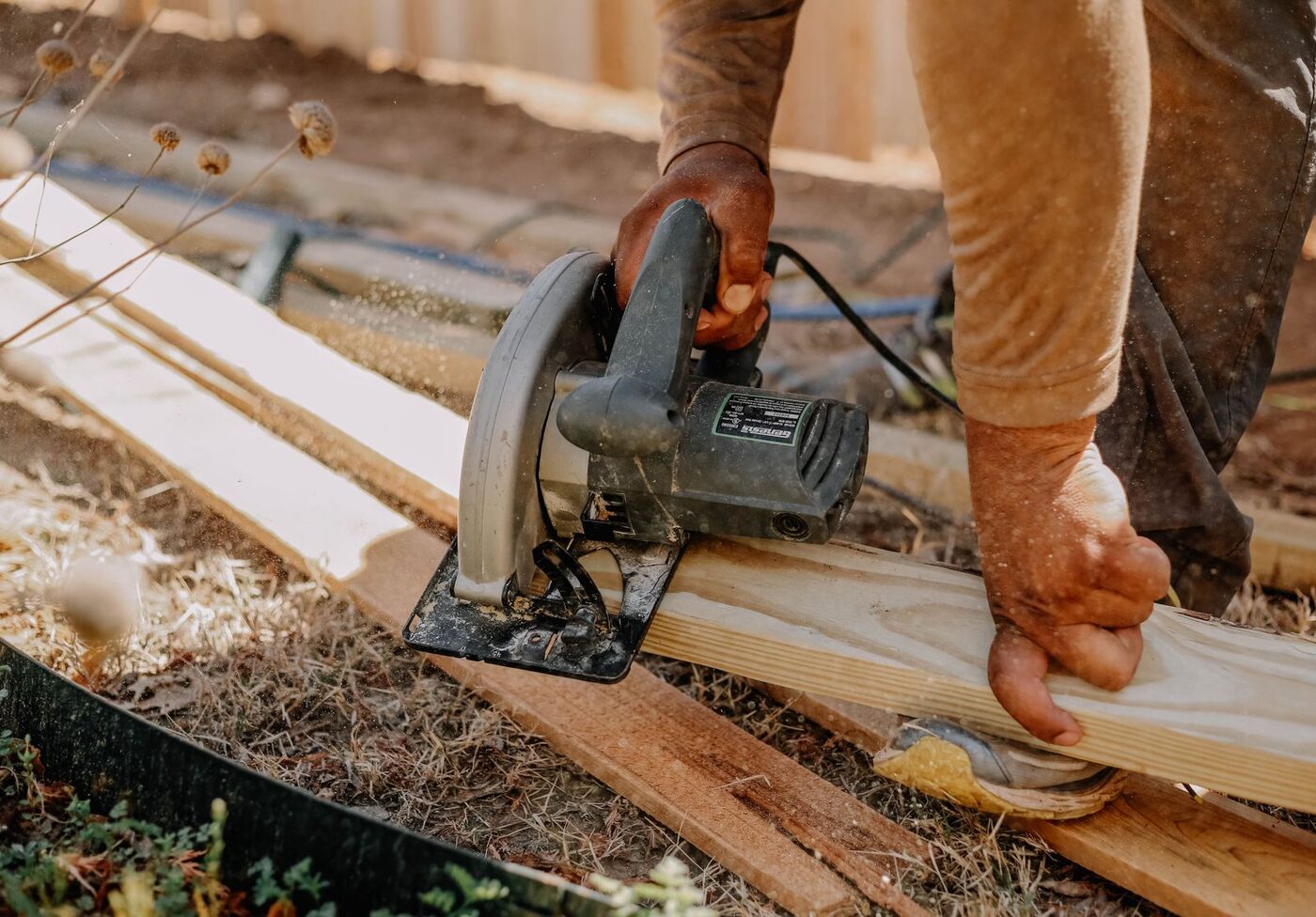 Circular saw cutting a length of timber held by a tradesperson outdoors