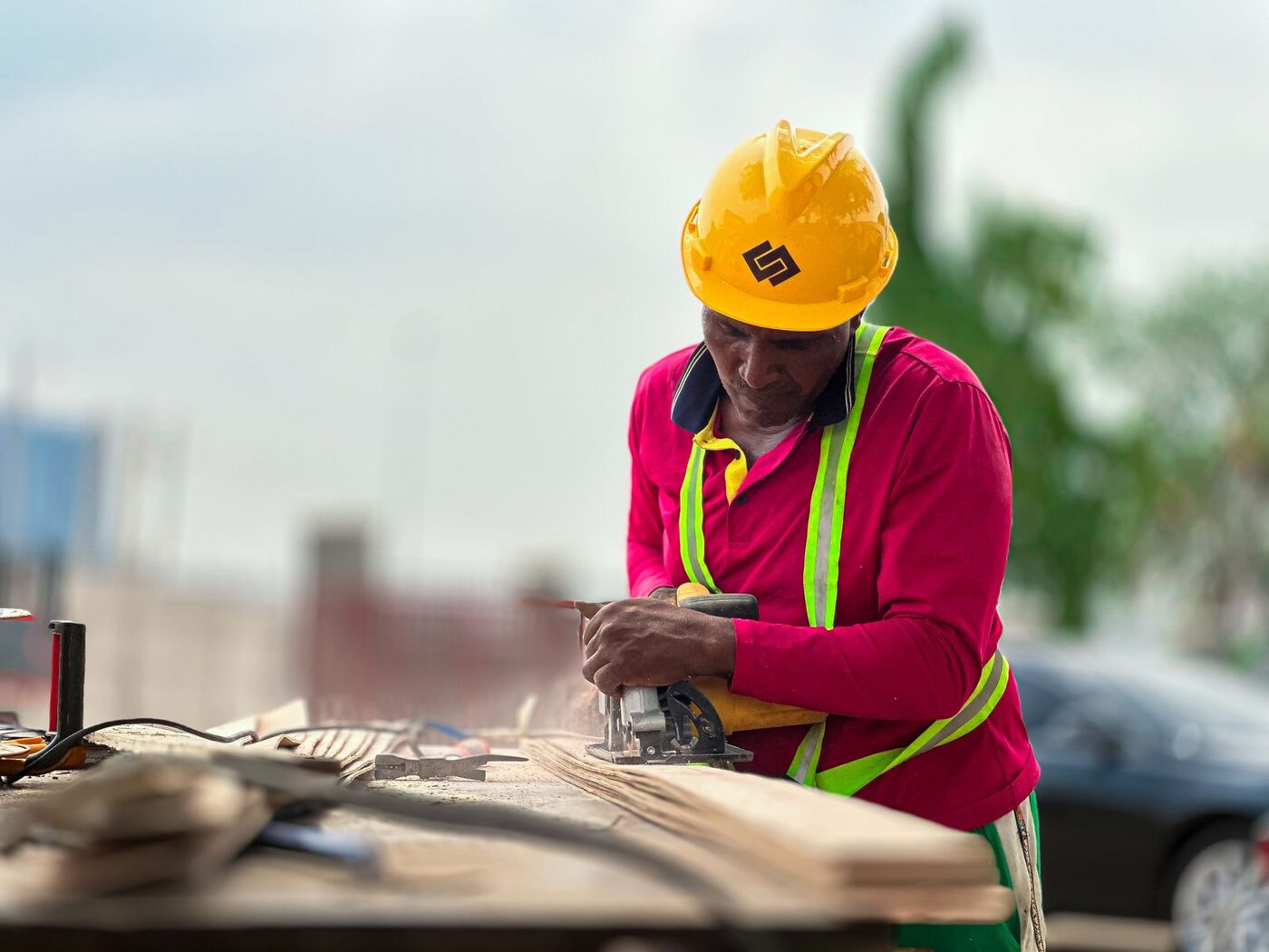 Tradesperson in hard hat and hi-vis cutting timber with a power tool